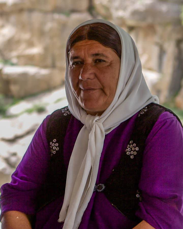 Mor geleneksel elbise ve işlemeli yelek giymiş kadın, kayalık fonda