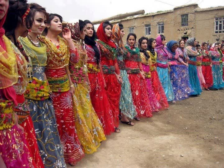 Sarı, kırmızı, mavi ve pembe pullu geleneksel Kürt elbiseleri giymiş kadınlar yan yana halay dizisinde