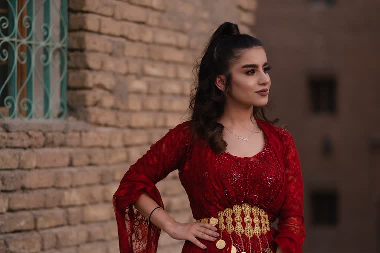 Kırmızı dantel işlemeli geleneksel elbise ve altın telkâri kemer takan genç kadın, Erbil Kalesi önünde