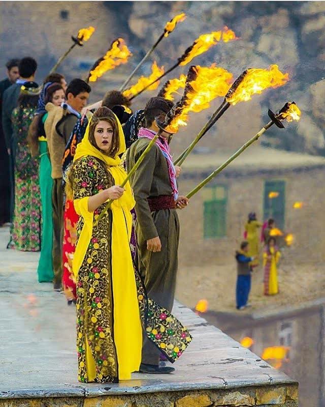 Sarı desenli goloni elbise ve başörtüsüyle elinde meşale taşıyan genç kadın, Palangan Newroz töreninde